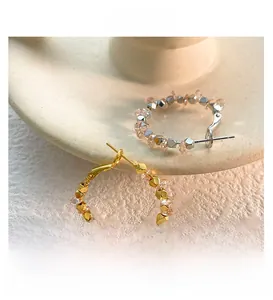 Dettaglio di orecchini a cerchio con perle metalliche sfaccettate oro e argento su ceramica
