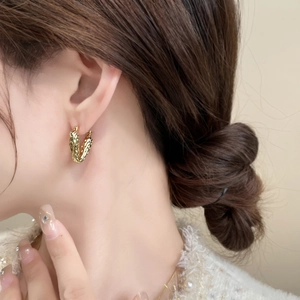 Detailed view of model wearing gold heart earrings with hammered geometric texture