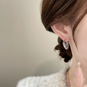 Detail of silver heart earring with hammered texture worn by a model in soft lighting