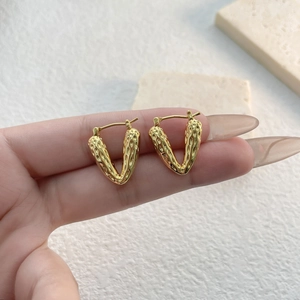 Gold-plated heart V-shape textured earrings held against a minimalist background
