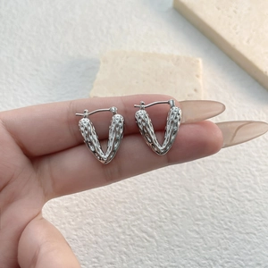 Detail of silver V-shaped hoop earrings with unique hammered texture held in hand