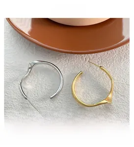 Détail des boucles d'oreilles créoles géométriques polies en or et argent sur pierre