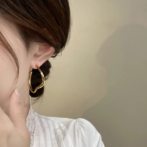 Boucles d'oreilles dorées irrégulières au design fluide portées avec éclairage doux
