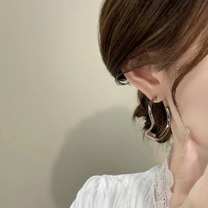 Gros plan de boucles d'oreilles créoles argentées ondulées et irrégulières sur un mannequin
