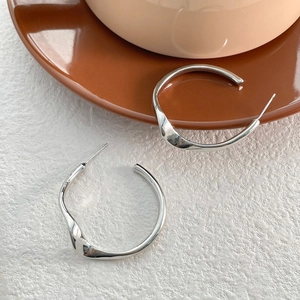 Gros plan de boucles d'oreilles C argentées ondulées avec finition polie et design