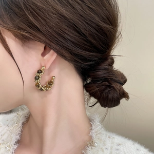 Gros plan de boucles d'oreilles créoles perlées dorées avec pierres d'oeil de tigre