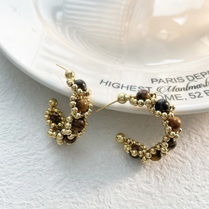 Détail des boucles d'oreilles créoles avec perles œil de tigre sur plateau blanc