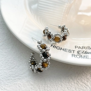 Gros plan de boucles d'oreilles en C avec pierres œil de tigre brunes et perles argentées