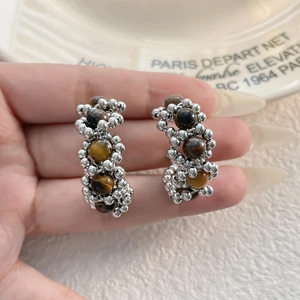 Gros plan de boucles d'oreilles créoles argentées avec perles œil de tigre et détails perlés
