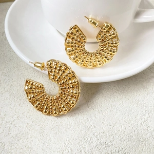Golden C-shaped earrings with textured metal beads on a ceramic cup background