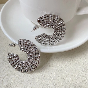 Detailed view of silver C-shaped earrings with textured bubble surface on a white saucer