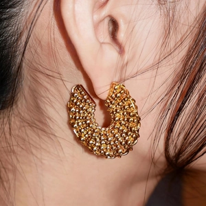 Close-up of gold-plated C-shaped earrings with textured spherical micro-beads on model