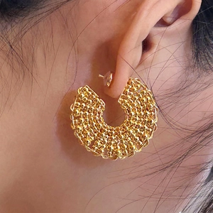 Macro detail of gold-plated C-shaped earrings with intricate beaded texture on ear