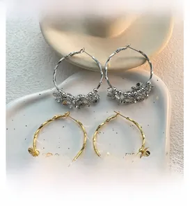 Detail view of gold and silver hoop earrings with metal flower charms on a ceramic plate