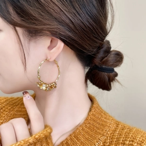 Detailed close-up of a large gold camellia flower hoop earring on a female model