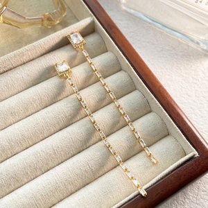 Détail de boucles d'oreilles dorées avec des pierres en zircone carrées et rectangulaires