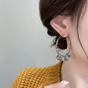 Silver camellia hoop earrings with textured floral clusters worn by a model
