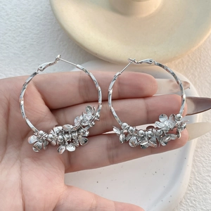 Detail of silver hoop earrings with diamond-set flower charms held by hand