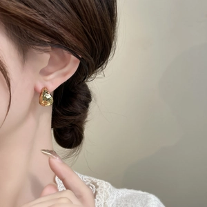 Close-up of hammered gold C-shaped earrings worn by a model for a chic minimalist look
