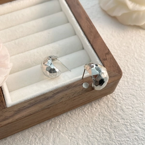 Macro shot of silver-colored hammered C-shaped earrings on a velvet jewelry stand