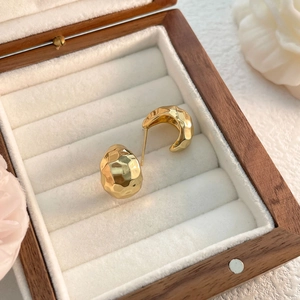 Detail of 18K gold plated C-shaped earrings with hammered texture in a wooden jewelry box