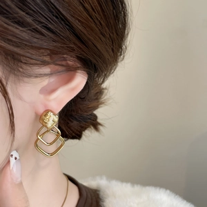 Detail of layered gold geometric earrings with textured square studs on female model