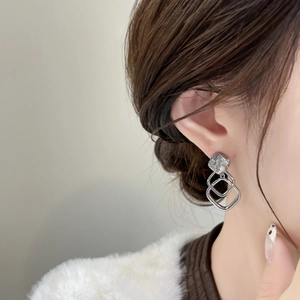 Detail of silver geometric square earrings featuring layered hollow shapes on model