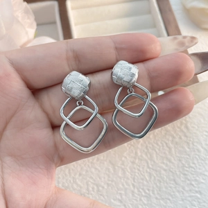 Detail of silver geometric earrings featuring textured square studs and hollow diamond drops