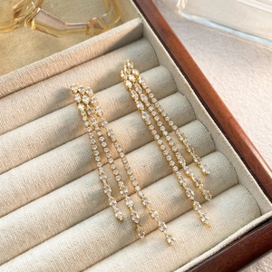 Detailed close-up of long gold fringe earrings with sparkling three-row zircon tassels
