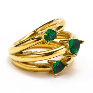 Anello geometrico multistrato in oro con zirconi verdi a forma di cuore su sfondo bianco