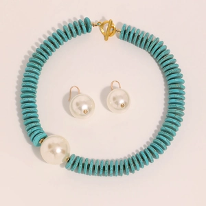 Detailed flat lay of turquoise disc necklace with large white pearls and gold T-bar clasp