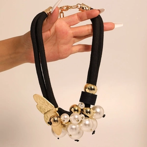 Statement necklace featuring golden butterfly pendant with pearls and black woven cords