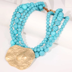 Détail d'un collier multi-rangs en perles turquoise avec grand pendentif doré martelé