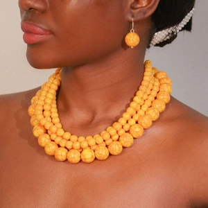 Detail view of multi-layer yellow acrylic beaded necklace with matching spherical earrings