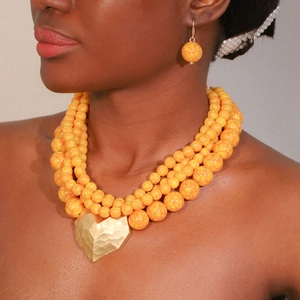 Macro detail of layered orange beaded necklace with large gold heart pendant and earrings