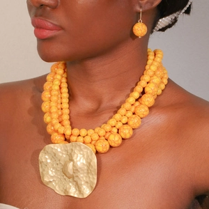 Detail of layered orange beaded necklace with a large gold hammered metal pendant
