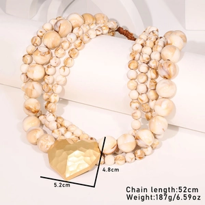 Detail of layered beaded necklace with large textured gold heart pendant and marble finish