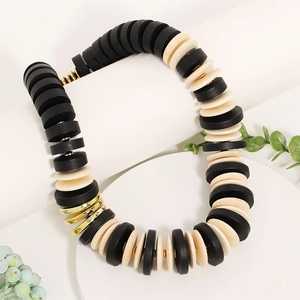Handmade beaded wooden necklace with black and gold discs on a white pedestal display