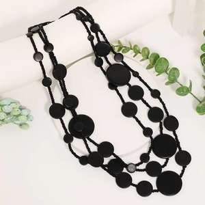 Artistic layered necklace with black matte beads and flat wooden disks on white props