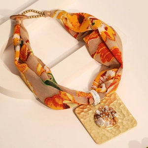 Detail of square hammered gold pendant with 3D flower charm on floral fabric strap