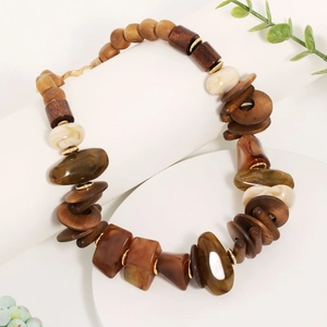 Bohemian handmade beaded necklace featuring wood, acrylic, and gold spacers on a white pedestal