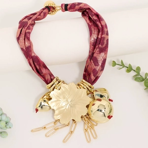 Macro detail of wine red fabric necklace with gold floral pendant and metal chain tassels