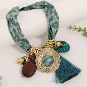 Détail d'un collier bohème avec pompon turquoise, imprimé léopard et disque en métal doré