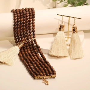 Parure bohème avec perles en bois sombre et pompons crème sur fond chaleureux