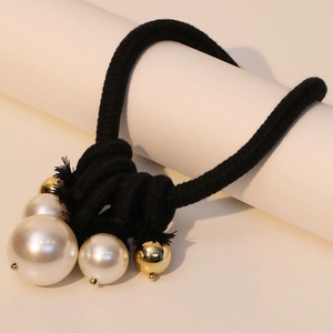 Artistic knotted black cord necklace with white faux pearls and gold beads on white pedestal