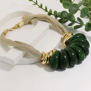 Detail of chunky gold chain necklace with emerald green resin teardrop beads on display
