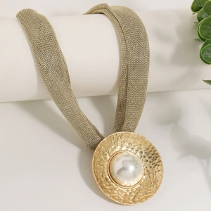 Detailed macro view of a gold mesh chain with hammered metal pendant and faux pearl inlay