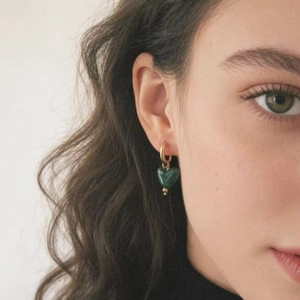 Boucles d'oreilles cœur en résine verte avec anneaux en acier doré portées par un mannequin