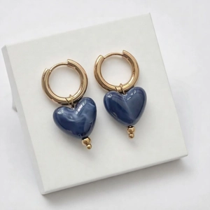 Détail de créoles dorées avec pendentifs en résine bleue en forme de cœur effet marbre