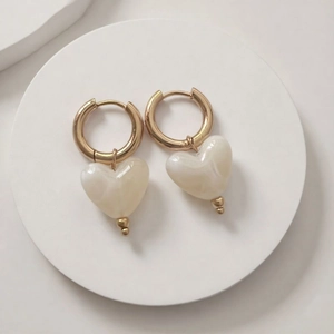 Détail des boucles d'oreilles cœur dorées avec pendentifs en résine marbrée sur pierre